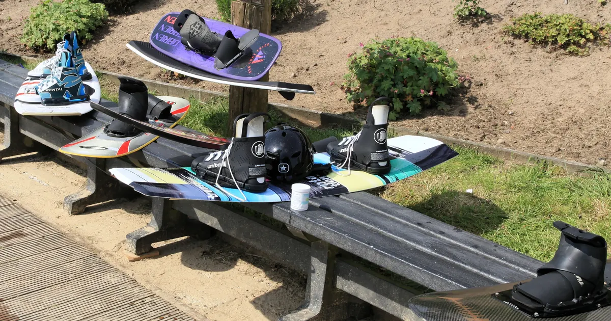 Rental wakeboards with bindings and a helmet laid out on a bench at a cable park, the gear to check before an Al Forsan wakeboarding session