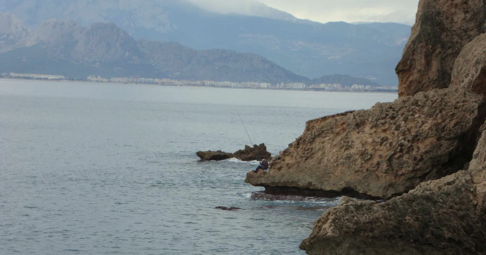Wave-cut limestone cliffs east of Antalya city centre with an angler on the rocks and the bay behind, the city coast with no no-dive box
