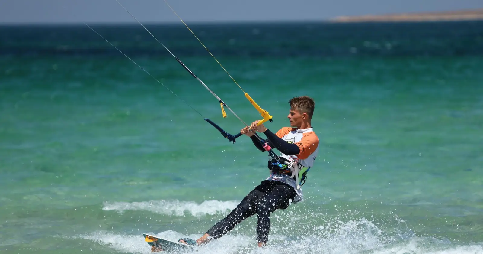 Kitesurfer carving across shallow turquoise flat water
