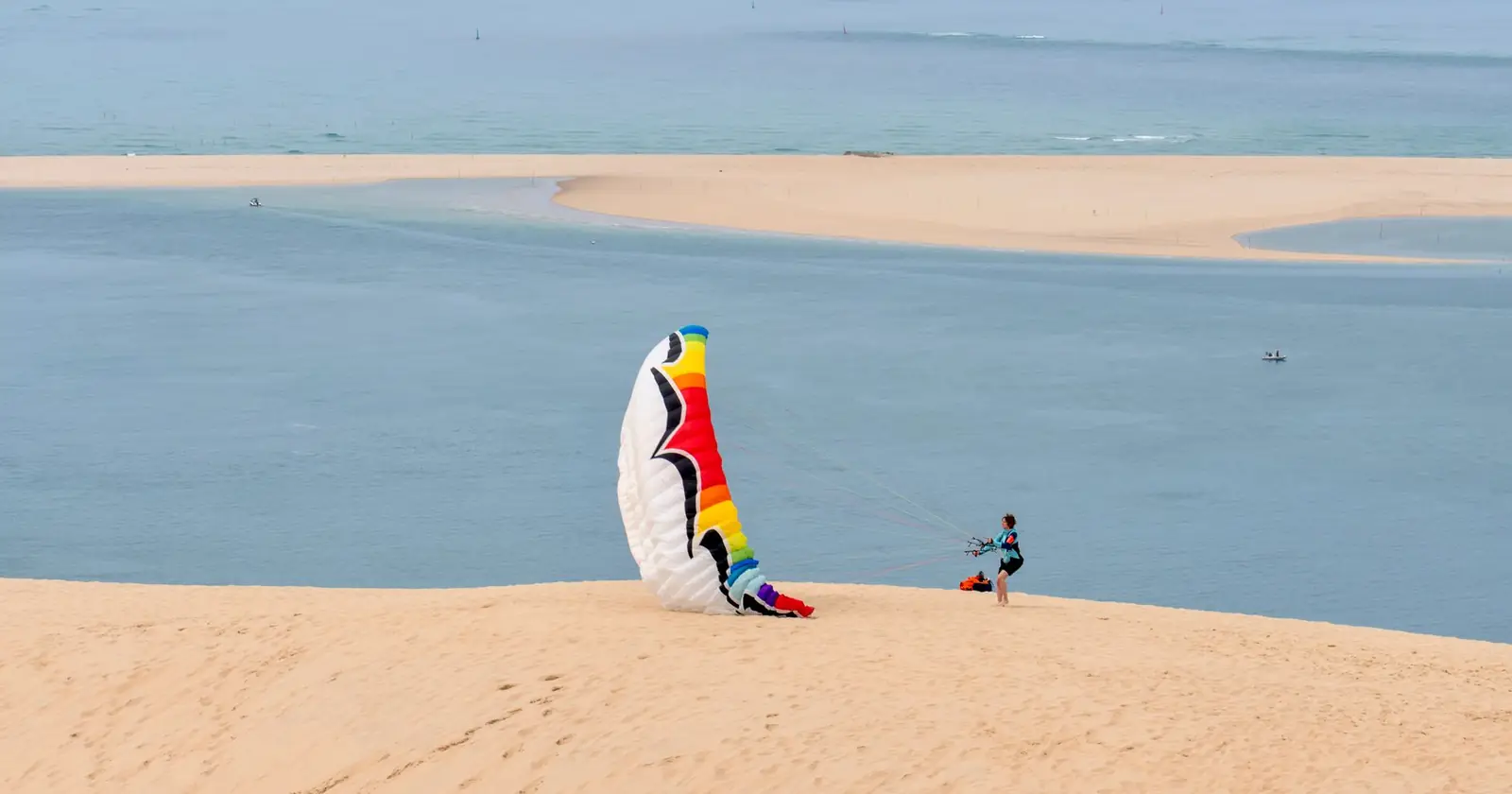 A paraglider prepares for takeoff on a scenic sandy dune by