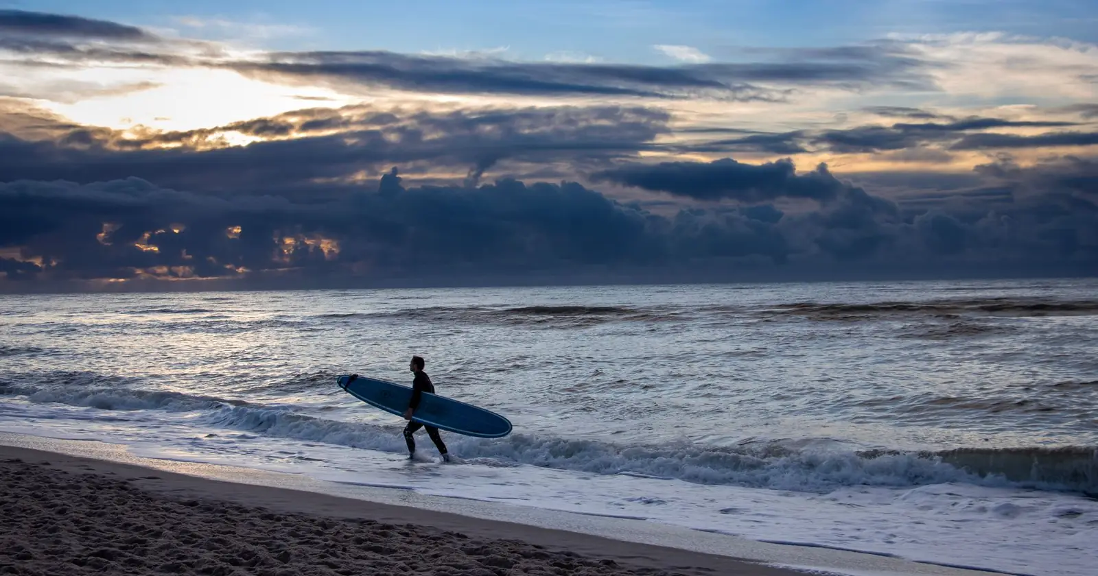 Silhouette of a surfer carrying a board along the beach duri