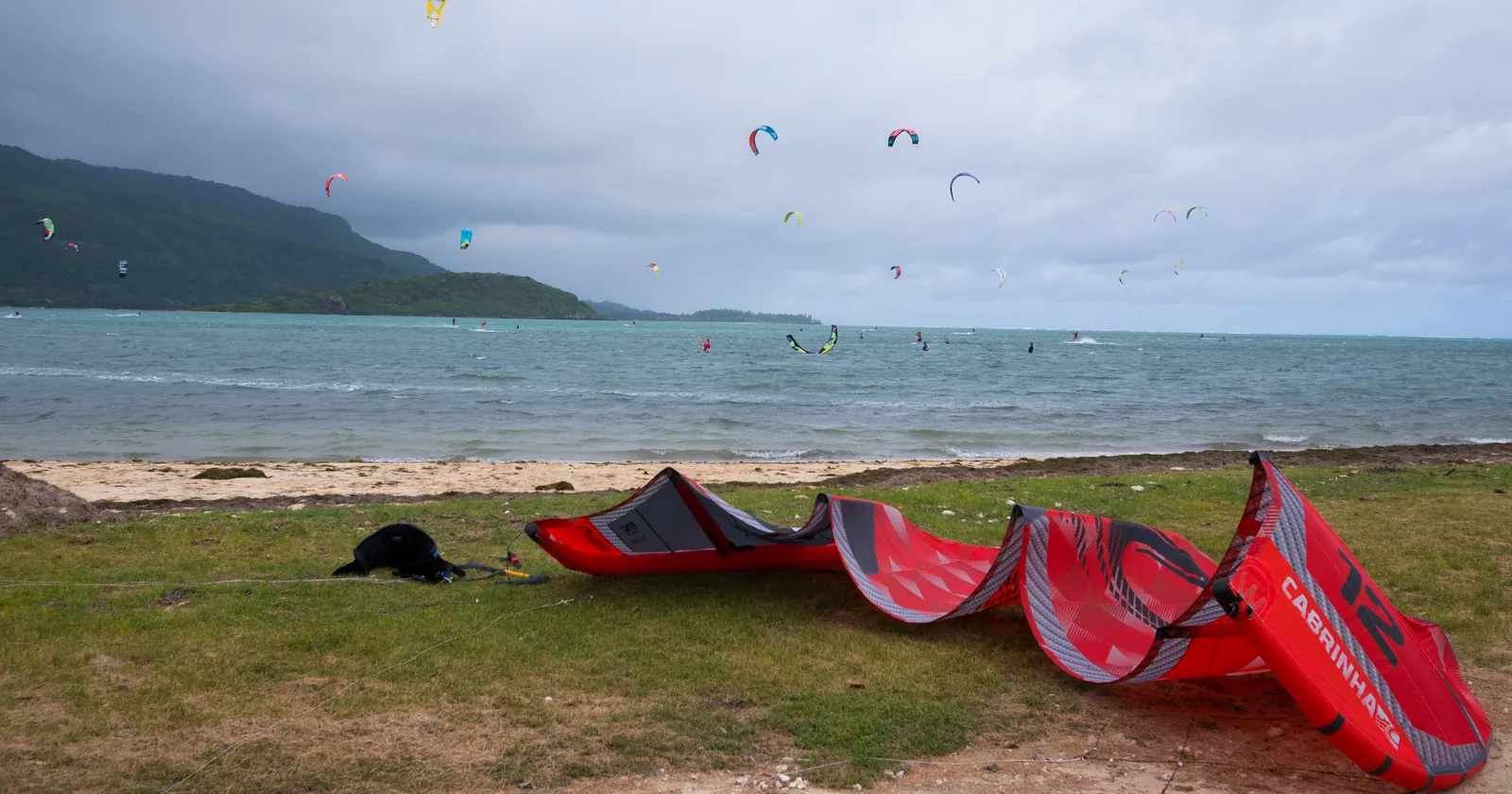 Kites over the lagoon at Le Morne, Mauritius, with a red kite laid out on the grass in front