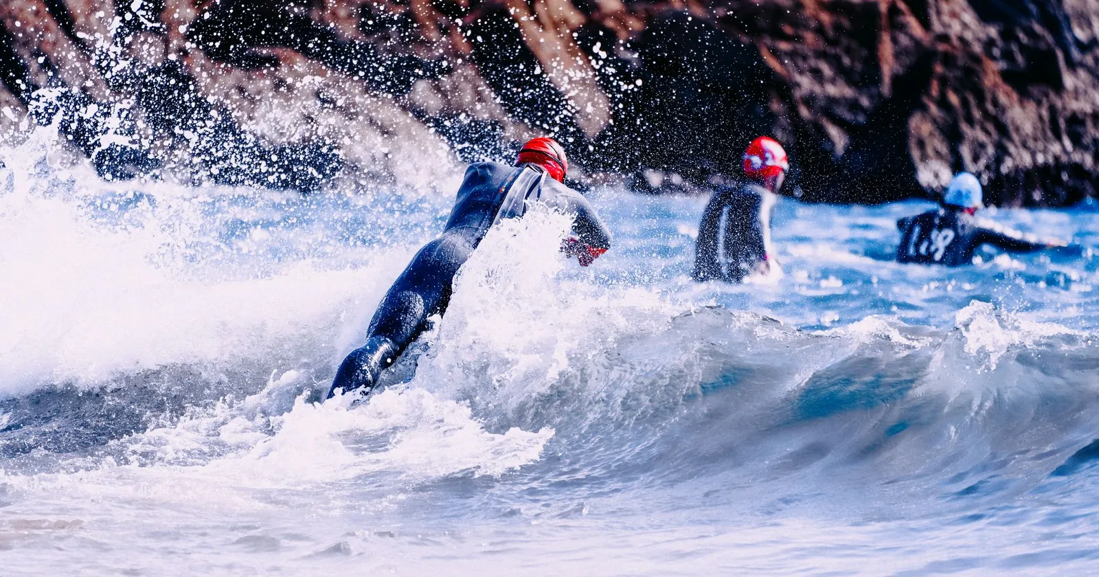 Coasteering group in wetsuits and helmets swimming beside cliffs