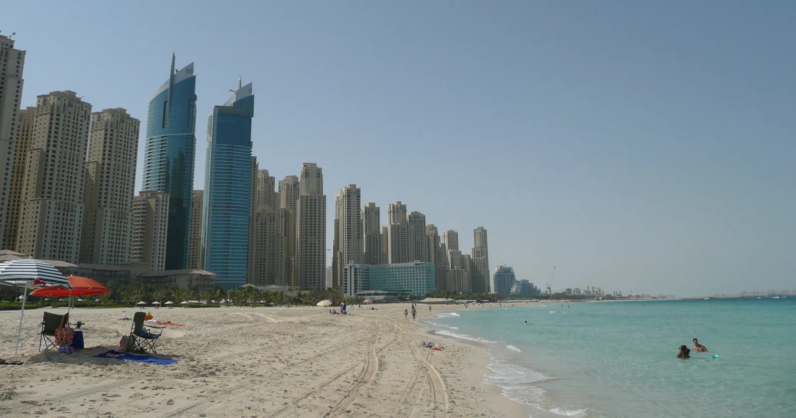 Public beach in the Dubai Marina area with swimmers in shallow water and the Jebel Ali port cranes on the horizon, the shoreline where Dubai diving from the beach starts