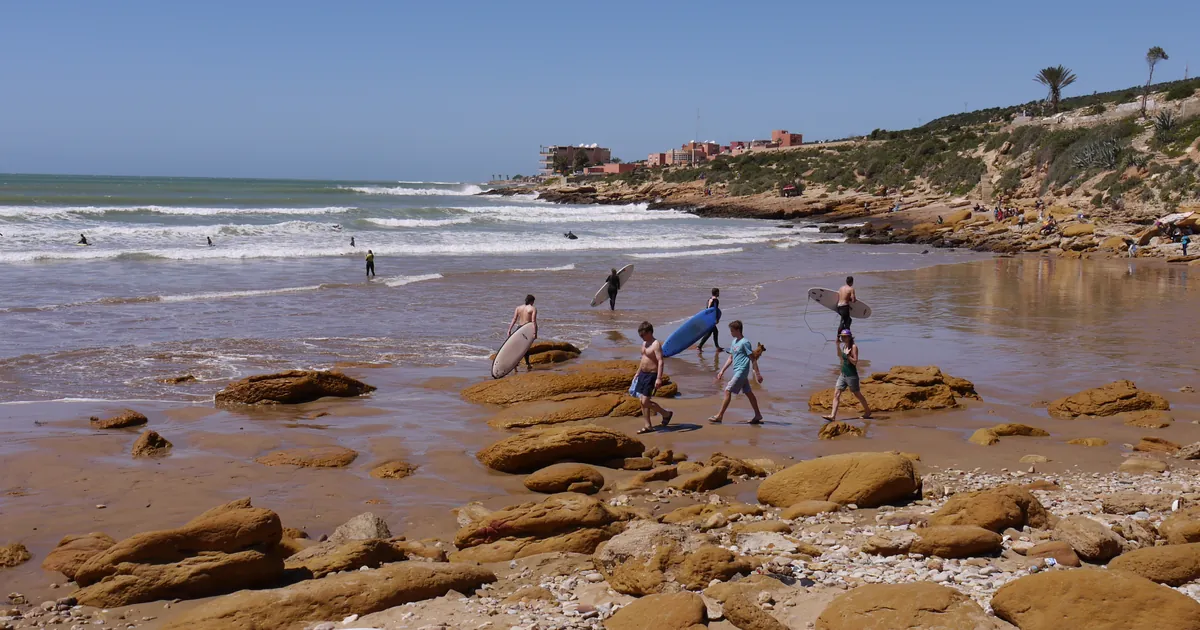 Surfers carrying boards over the rocks into the waves at a beach near Taghazout