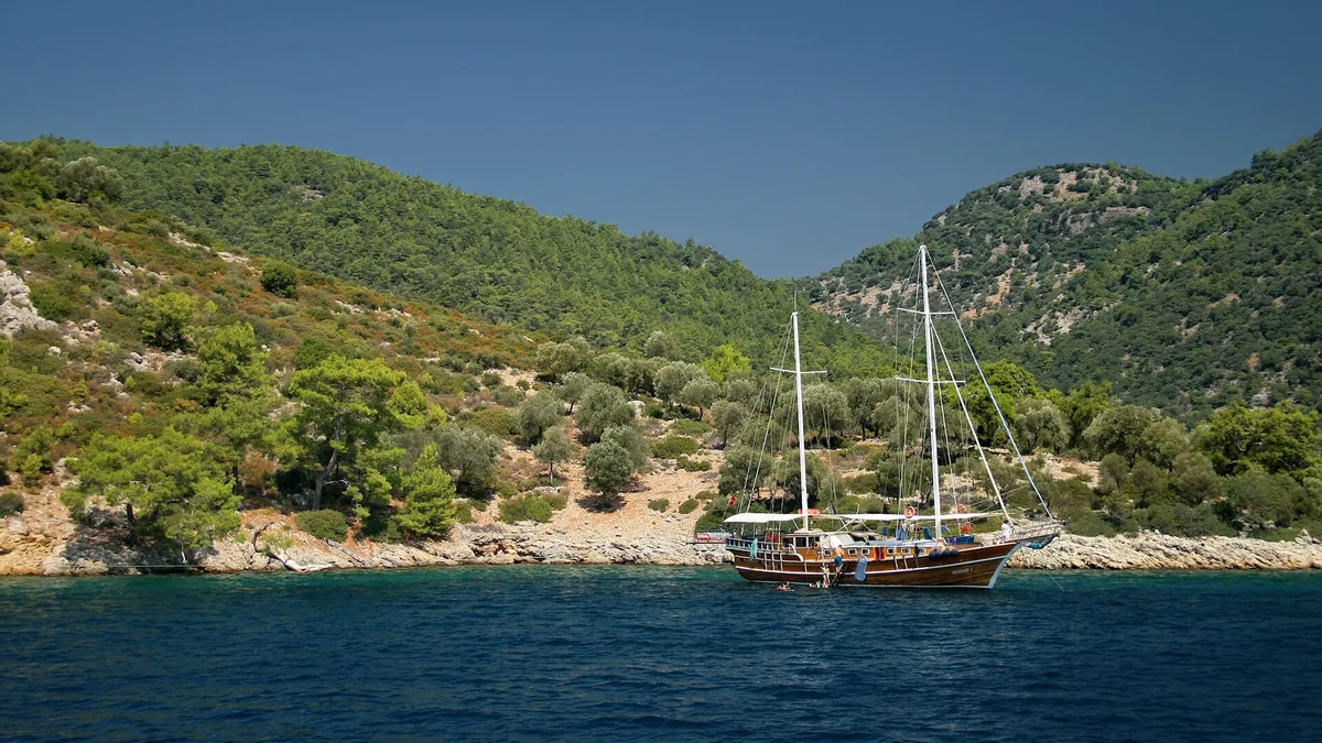 A gulet tied stern-to by lines to the wooded shore of Sarsala bay in the Gulf of Göcek near Fethiye, a cove that lies inside the closed diving box A6