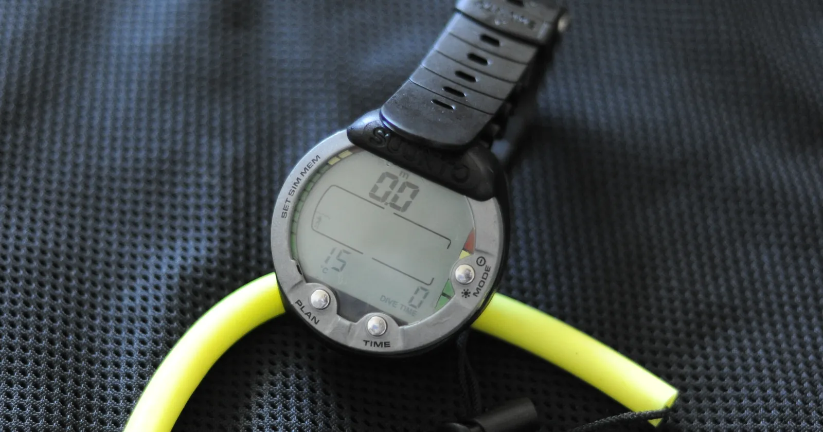 Older Suunto Vyper puck-style dive computer with a yellow bungee mount