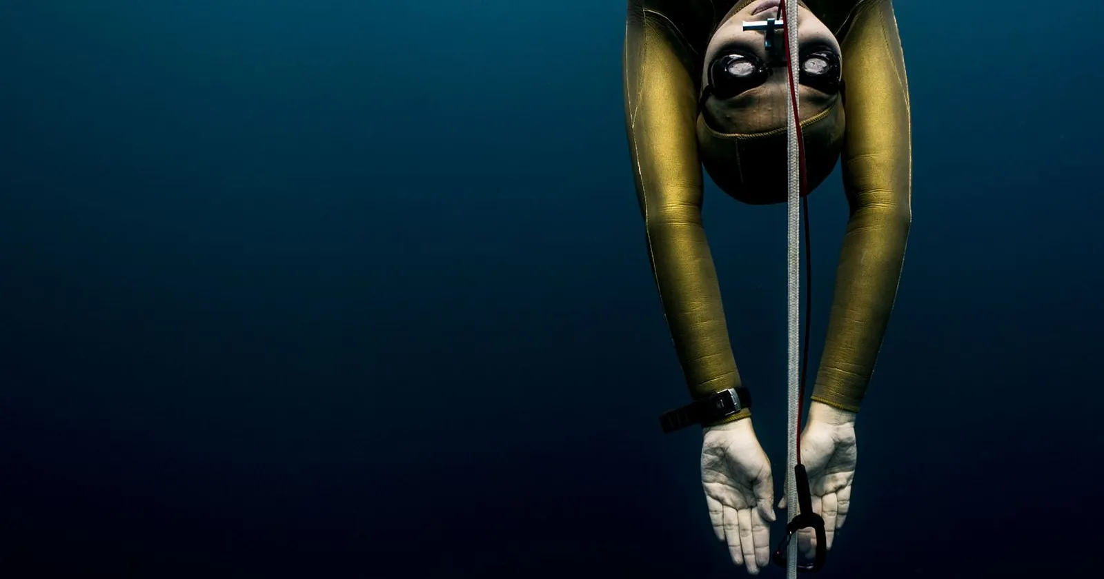 Freediver gliding beside a sunlit reef wall on a single breath