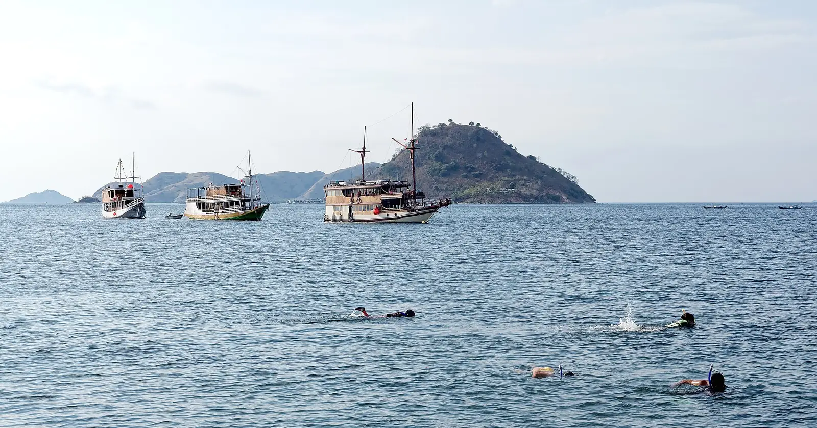 Snorkellers off Flores, Indonesia, with liveaboard boats anchored behind