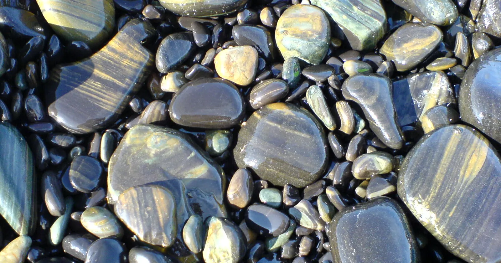 Smooth striped black stones on the beach of Koh Hin Ngam, a Tarutao park island near Koh Lipe diving sites where stacking stones is banned