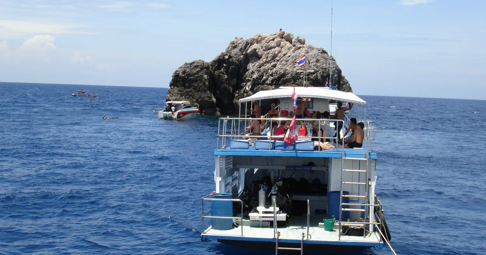 A Koh Samui diving day boat tied off beside Sail Rock, the granite pinnacle called Hin Bai, with a speedboat and snorkelers behind it