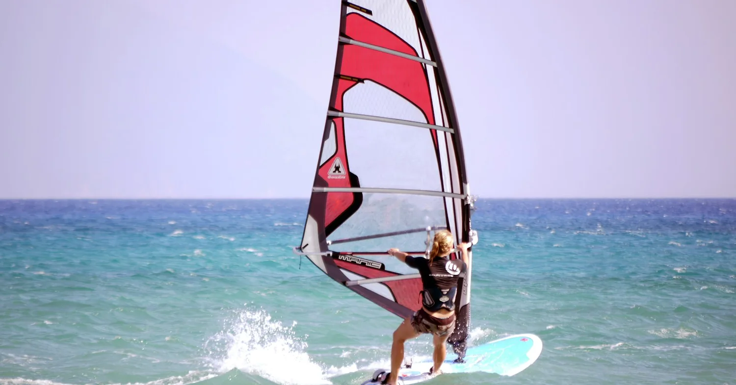 A kitesurfer riding flat shallow water off a wide sandy beach on a Greek island coast