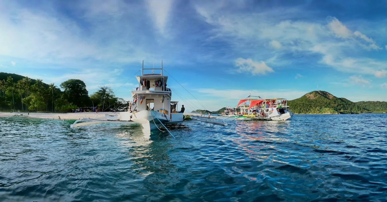 Clear shallow water over coral and sand off a forested tropical island close to a city coastline