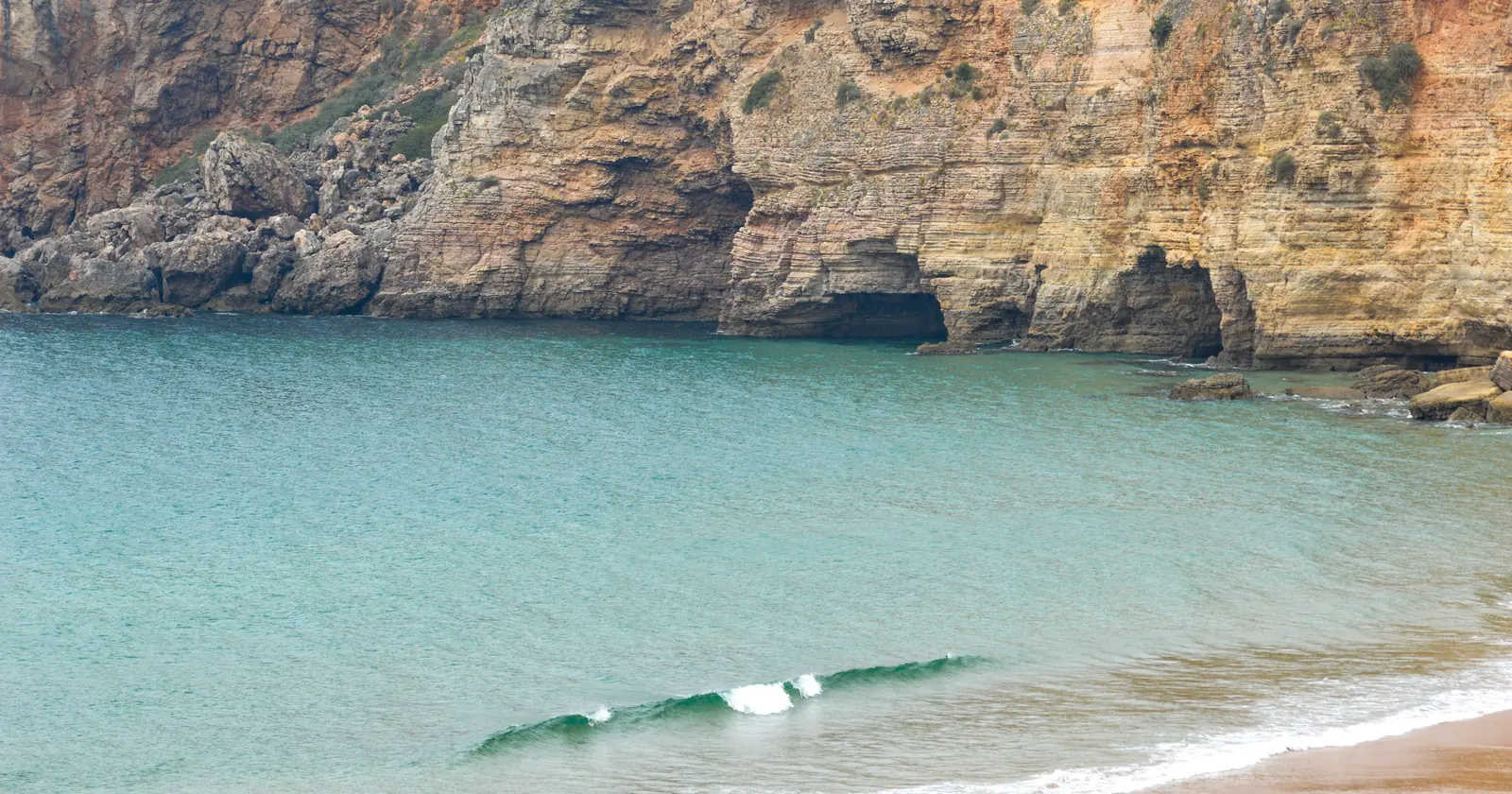 Small wave breaking below the cliffs at Praia do Beliche near Sagres