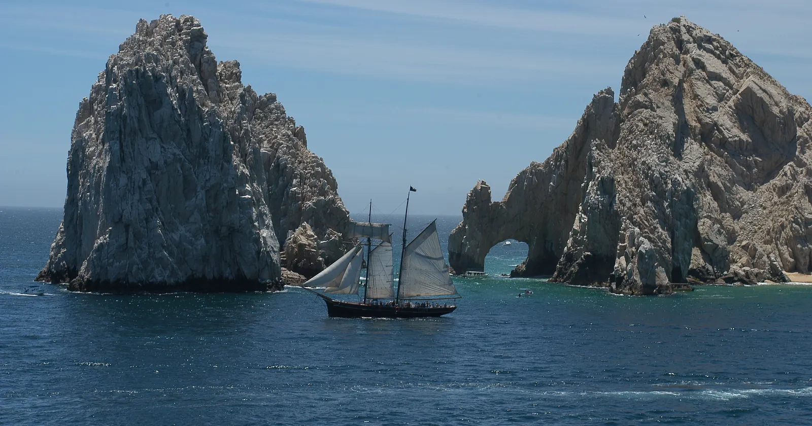 A two-masted sailing ship passing the Arch of Cabo San Lucas and the rock beside it, inside the protected area where most Los Cabos diving at Land's End takes place