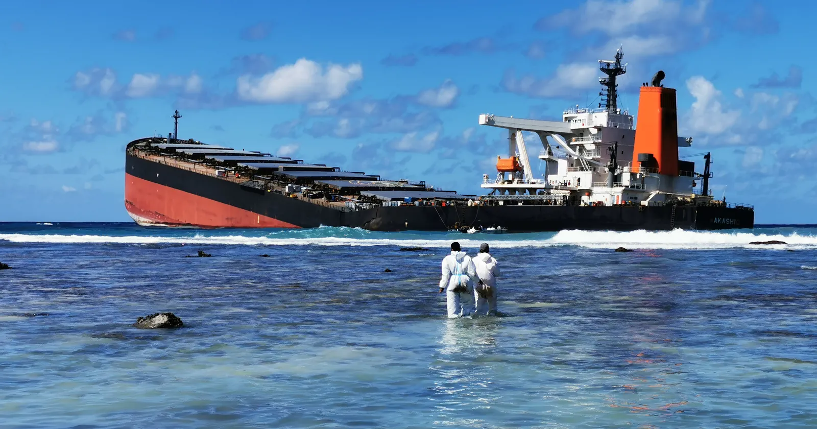 Two responders in protective suits wade toward the MV Wakashio on the reef off Pointe d'Esny, the grounding site covered in this Mauritius diving guide, 13 August 2020
