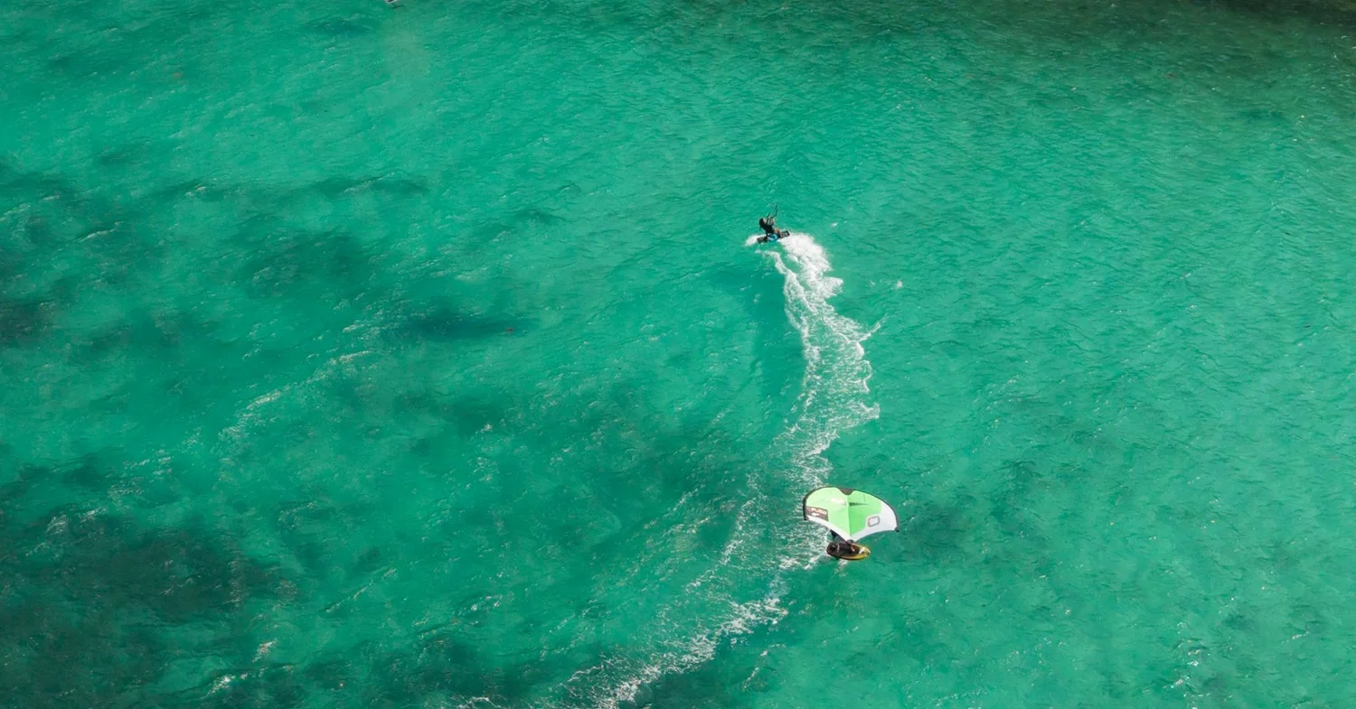 A kitesurfer on flat turquoise water off a wide sandy beach in the Cyclades
