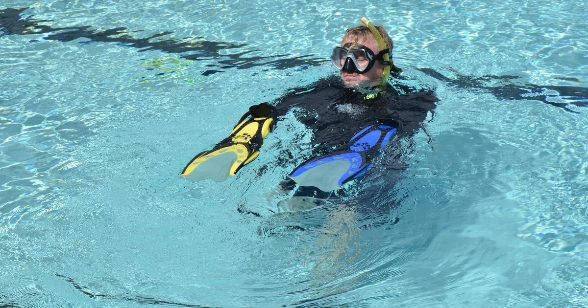 Open Water student in mask, snorkel and fins practising in a pool, the confined-water stage of both the PADI and SSI course