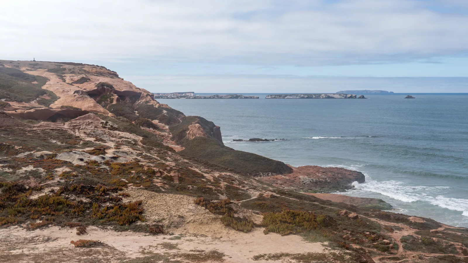 The coast at Peniche, Portugal, with the peninsula and town in the distance and swell breaking along the rocks