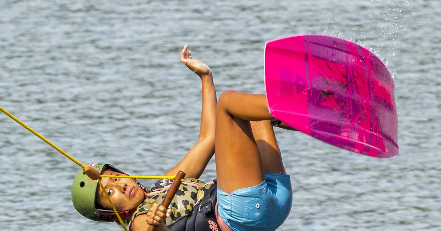 Cable wakeboarding rider in helmet and impact vest upside down above the water, holding the cable handle, the gear the Phuket Wake Park ticket includes