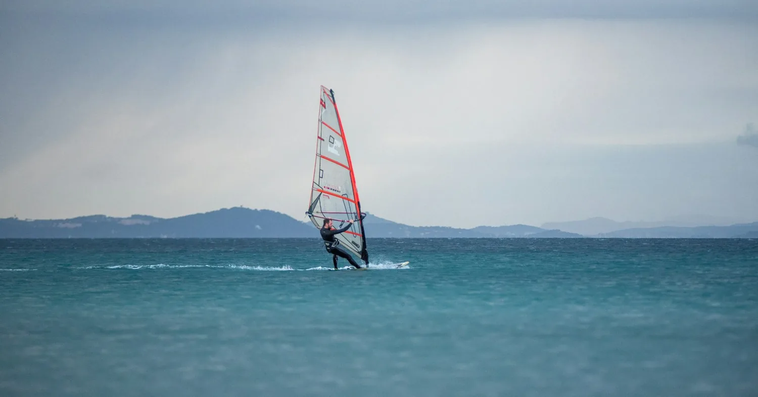 A windsurfer planing on turquoise Mediterranean water off a Greek island coast