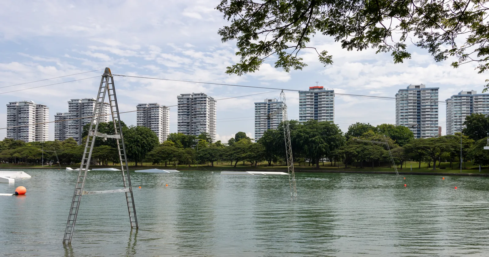 A cable tower and floating obstacles on the lagoon at East Coast Park in Singapore, with residential towers behind the treeline