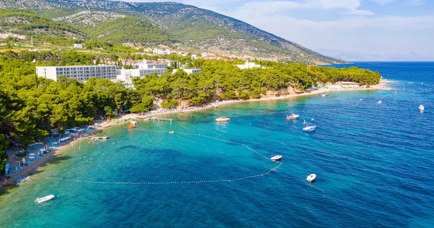 Aerial view of the shore at Bol on the island of Brac, a Split diving destination, with swimming-zone buoy lines over sand and darker patches of seabed