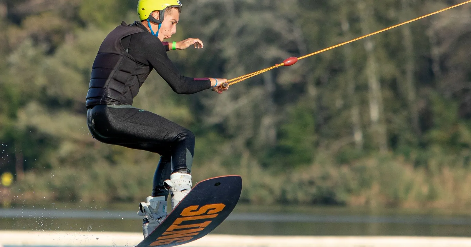 Wakeboarder wearing a helmet and impact vest at a cable park